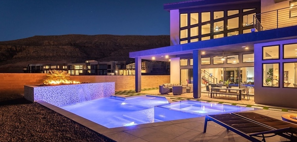 A glowing backyard pool and spa at night